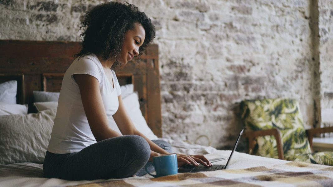 A woman working on a laptop in bed.